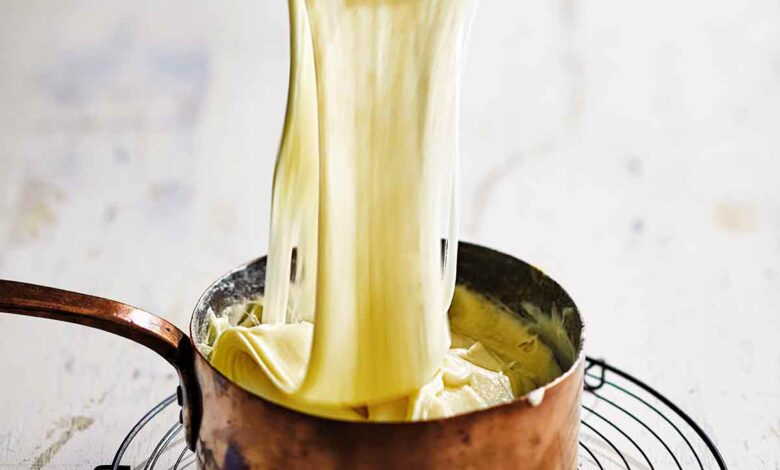 A person scooping cheesy aligot potatoes from a copper saucepan set on a wire rack.