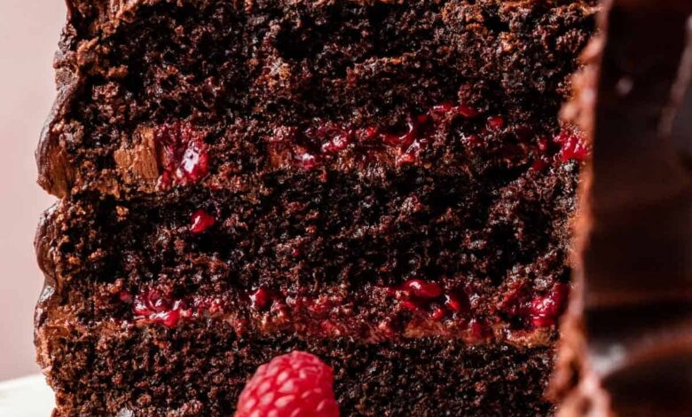 chocolate raspberry cake cut open with raspberries and mint on top sitting on a marble cake stand with pink backdrop behind it.