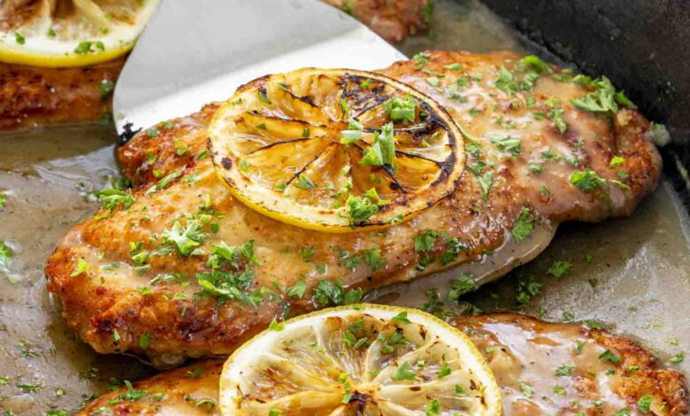 side view shot of chicken francese in a pan, with one being picked up by a spatula.