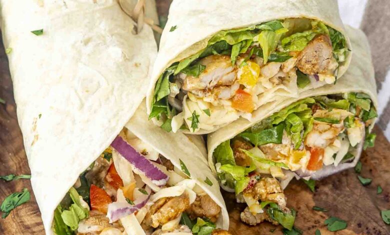 Chipotle Chicken Wraps on a rustic wooden board, cut open to reveal juicy chicken, crisp lettuce, red onion, bell peppers, and melted cheese, garnished with fresh cilantro.