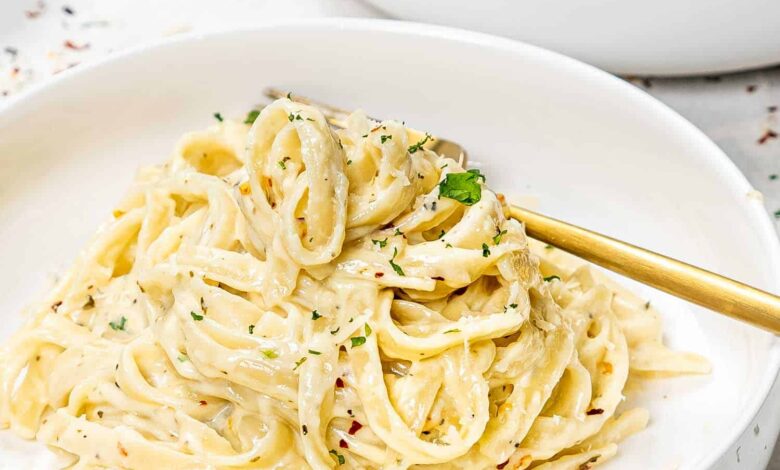 a serving of fettuccine alfredo in a white bowl with a golden fork.