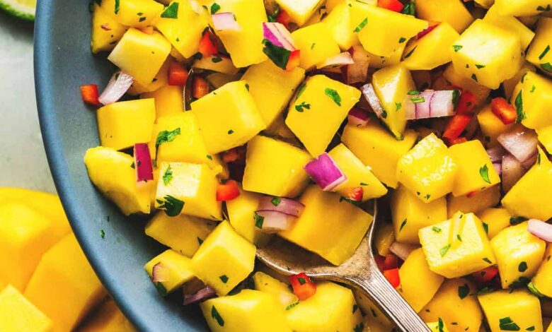 spoon dipping into bowl of diced mangoes with onions and cilantro