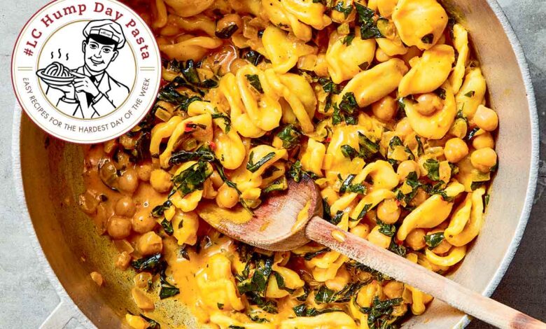 Orecchiette with chickpeas, turmeric, and greens in a large pot with a wooden spoon, on a countertop.