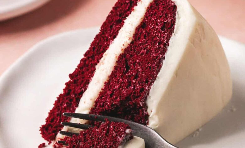 fork cutting into slice of layer cake with cream cheese frosting on plate