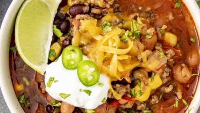 A bowl of taco soup topped with melted cheese, sour cream, sliced jalapeños, and fresh cilantro, served with a lime wedge on the side.