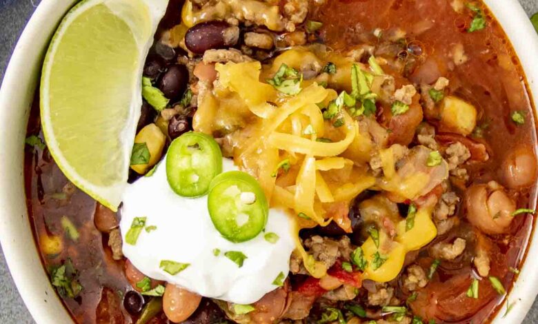 A bowl of taco soup topped with melted cheese, sour cream, sliced jalapeños, and fresh cilantro, served with a lime wedge on the side.