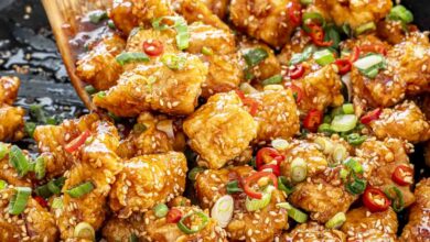 A wooden spoon tossing Korean fried chicken in a skillet