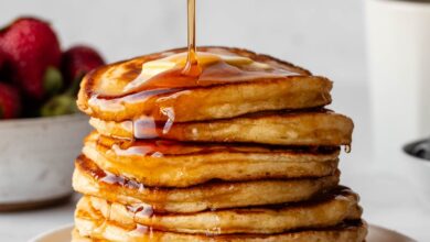 pouring maple syrup on a stack of pancakes.