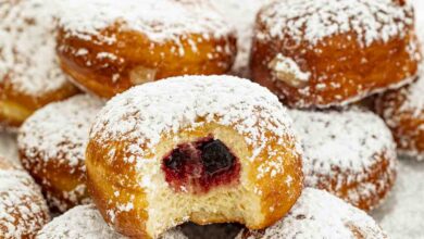 paczki dusted with powdered sugar with a bite taken out of one.