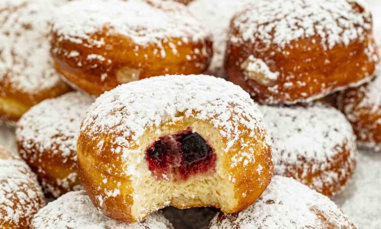 paczki dusted with powdered sugar with a bite taken out of one.